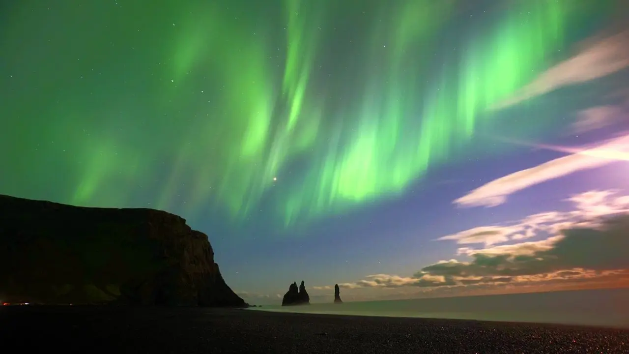 Zorza polarna nad plażą Reynisfjara i skalnymi iglicami Reynisdrangar koło Víku